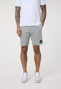 Pilki medvilniniai šortai su juodu logotipu, šoninėmis kišenėmis ir elastingu juosmeniu, derinami su balta marškinėliais ir baltais batais.