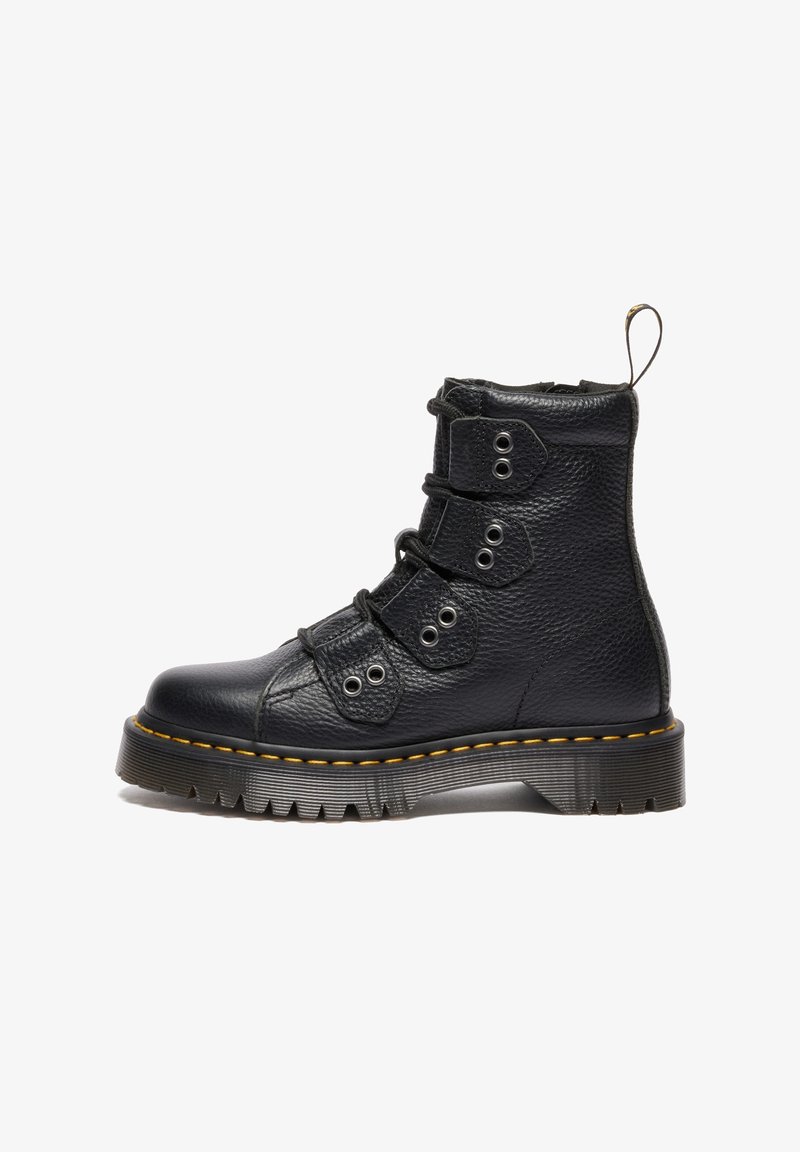 Botte de combat en cuir noir avec une semelle épaisse à crampons, une couture jaune et quatre sangles avec œillets métalliques pour les lacets, vue de profil.