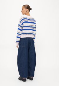 Overdimensjonert stripet genser i blå, hvit og rosa garn; kombinert med vide mørkeblå jeans; svarte kraftige støvler synlige.