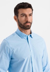 Camicia azzurra chiaro con bottoni, realizzata in un tessuto morbido, con colletto classico e maniche lunghe, caratterizzata da una finitura testurizzata.