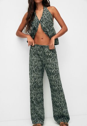 Femme portant un top dos nu vert et beige imprimé animalier avec un pantalon large assorti sur fond blanc.