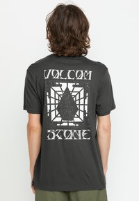 Sort bomulds T-shirt med et stort hvidt grafisk design på ryggen, der viser en diamantform i et netlignende mønster.