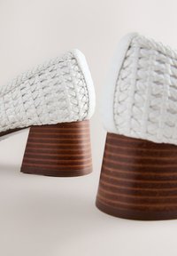 Witte leren schoenen met een geweven textuur, voorzien van een stevige bruine gestreepte hak voor extra hoogte en stabiliteit.