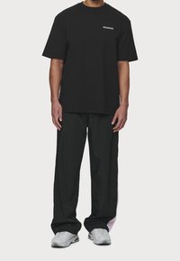 Černé tričko s potiskem "PEGADOR" na levé hrudi, s volnými černými kalhotami s růžovým akcentem a šedými teniskami.