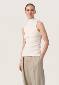 Weißes, geripptes, ärmelloses Rollkragenoberteil mit tailliertem Design, kombiniert mit weit geschnittenen beigen Hosen. Glatte Textur, klare Linien, minimalistischer Stil.