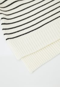 Sciarpa lavorata a maglia di colore crema con strisce orizzontali nere. Texture a costine, ripiegata su un'estremità, mostrando il tessuto a strati.