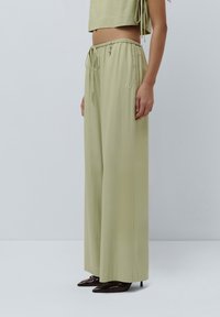 Pantaloni a gamba larga verde chiaro con vita regolabile, caratterizzati da una texture liscia e dettagli ricamati discreti.