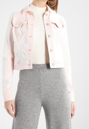 Femme portant une veste en jean courte rose clair sur un top blanc côtelé et un pantalon large gris taille haute sur fond blanc.
