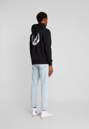 Must musta, mille seljal on ümmargune graafika, koos heledate teksaste ja valgete kõrge nike kingadega. Sile tekstuur, lõdvestunud istuvus.