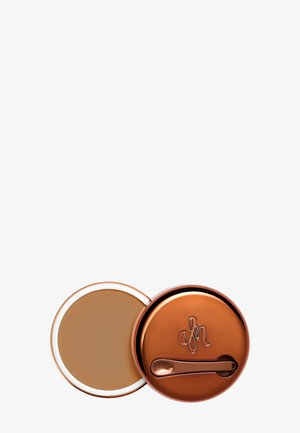 Bronze-colored compact with a mirrored lid, containing cream foundation. Features a small spatula for application and a smooth texture.