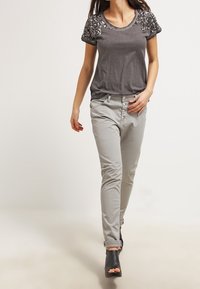 Camiseta gris con hombros adornados con lentejuelas, combinada con pantalones gris claro y zapatos de tacón abiertos negros.