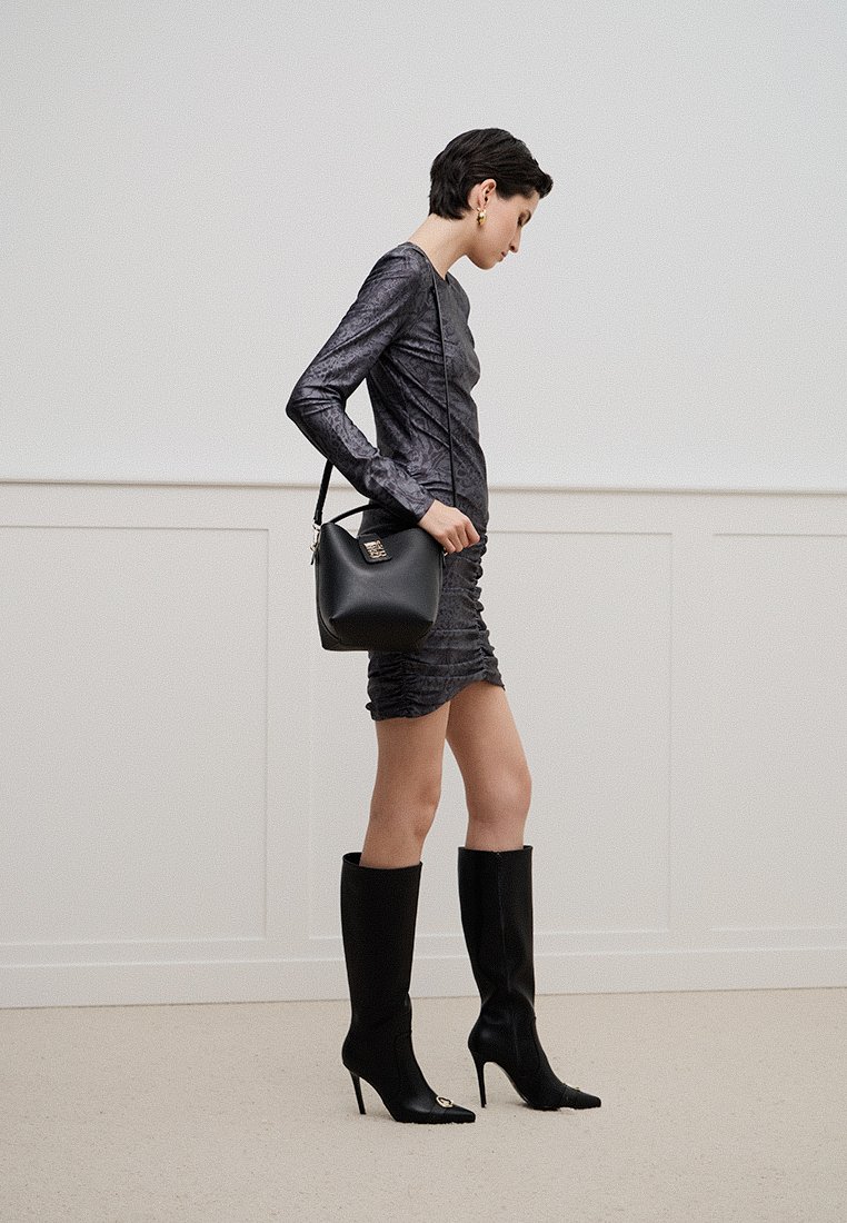 Robe noire texturée à manches longues, au design ajusté. Sac à épaule en cuir noir, bottes noires à talon haut jusqu'aux genoux, et détails en métal doré.