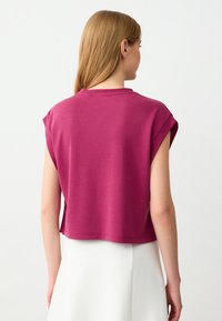 Top accorciato fucsia con maniche corte, caratterizzato da un collo rotondo e una vestibilità rilassata, realizzato in un tessuto morbido. Nessun motivo o accento visibile.