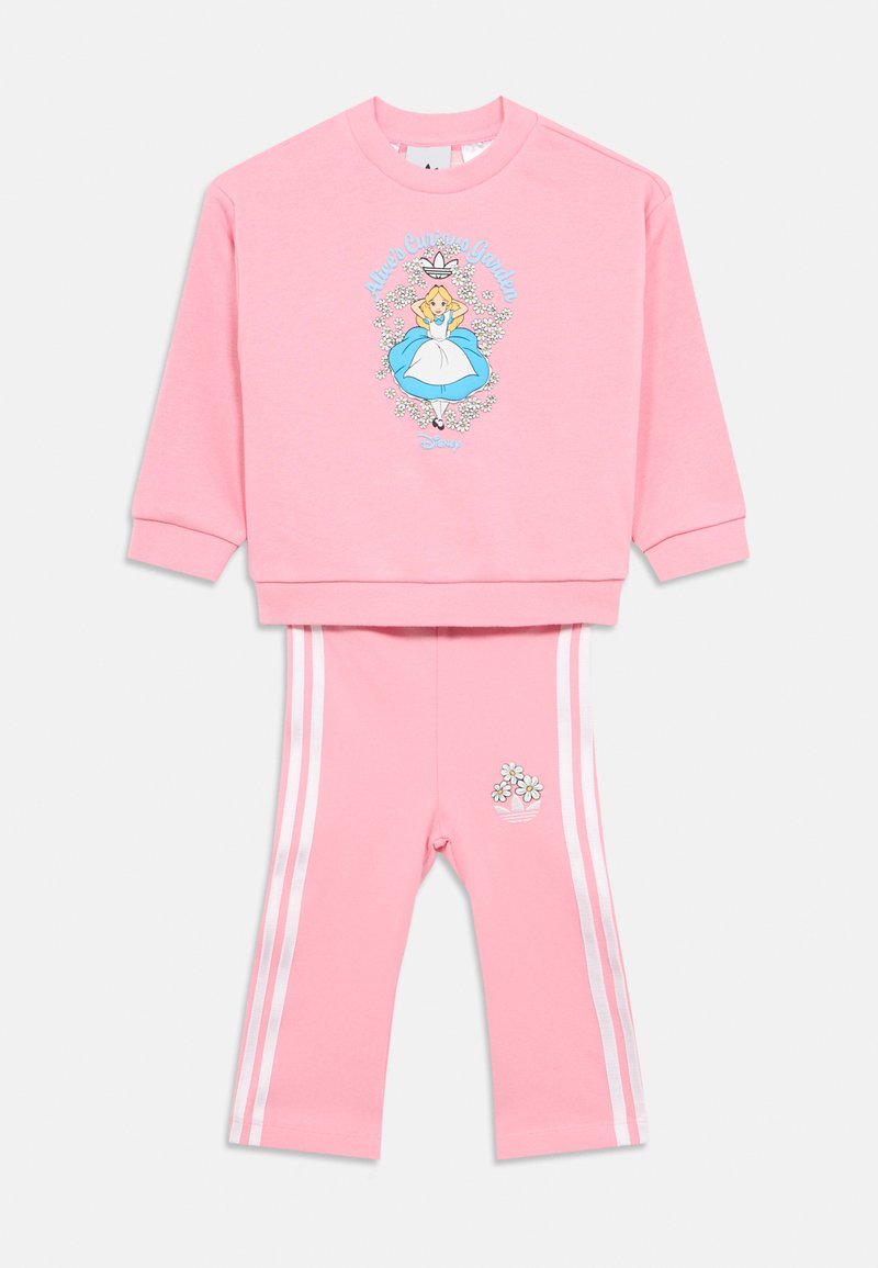 Rozā kokvilnas džemperis un saskaņotas legingi ar grafiku, kurā attēlota meitene zilā kleitā, ieskauta ziedos un svītrainos akcentos.