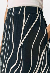 Jupe noire avec des rayures verticales beige, en tissu léger et texturé. Comprend des poches latérales et une taille lisse.