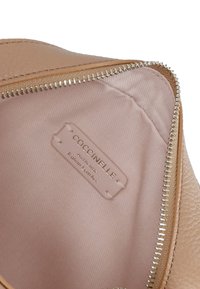 Interno di una borsa in pelle rosa chiaro con una cerniera beige. Presenta un'etichetta con la scritta "COCCINELLE Pelle Italiana Autentica" in testo dorato.