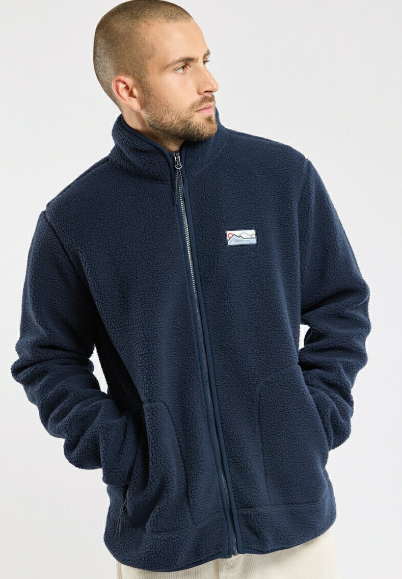 Veste en polaire bleu marine avec un col haut, fermeture éclair sur le devant, deux poches avant et un petit patch logo représentant des montagnes sur la poitrine gauche.