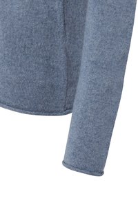 Gros plan sur une manche de pull en laine tricotée bleu clair et sur la couture latérale, montrant un tissu en laine doux et texturé.