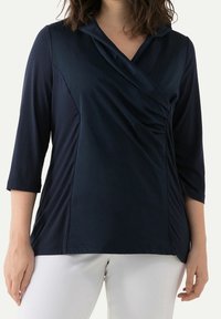 Top blu navy con maniche a ¾ e scollo drappeggiato. Presenta pannelli laterali testurizzati e un tessuto morbido per una silhouette aderente.
