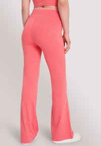 Uitlopende broek in felroze stof met een zachte textuur. Hoge tailleband met een subtiele logo en een schone zoom aan de onderkant.