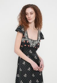 Μαύρο φόρεμα με κεντήματα λουλουδιών σε κόκκινο και άσπρο, με κοντά μανίκια με βολάν, τετράγωνη λαιμόκοψη και υφή με πουά.