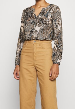 Blusa a maniche lunghe con scollo a V e stampa paisley in tonalità di marrone, crema e blu. Abbinata a pantaloni larghi a vita alta color beige.
