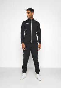 Survêtement de sport noir avec accents blancs et veste zippée. Présente un design ajusté, une texture lisse et un tissu léger.