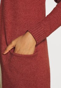 Stickad cardigan i en rik kastanjefärg, med ribbade ärmslut och en framficka, med en mjuk textur och en avslappnad design.