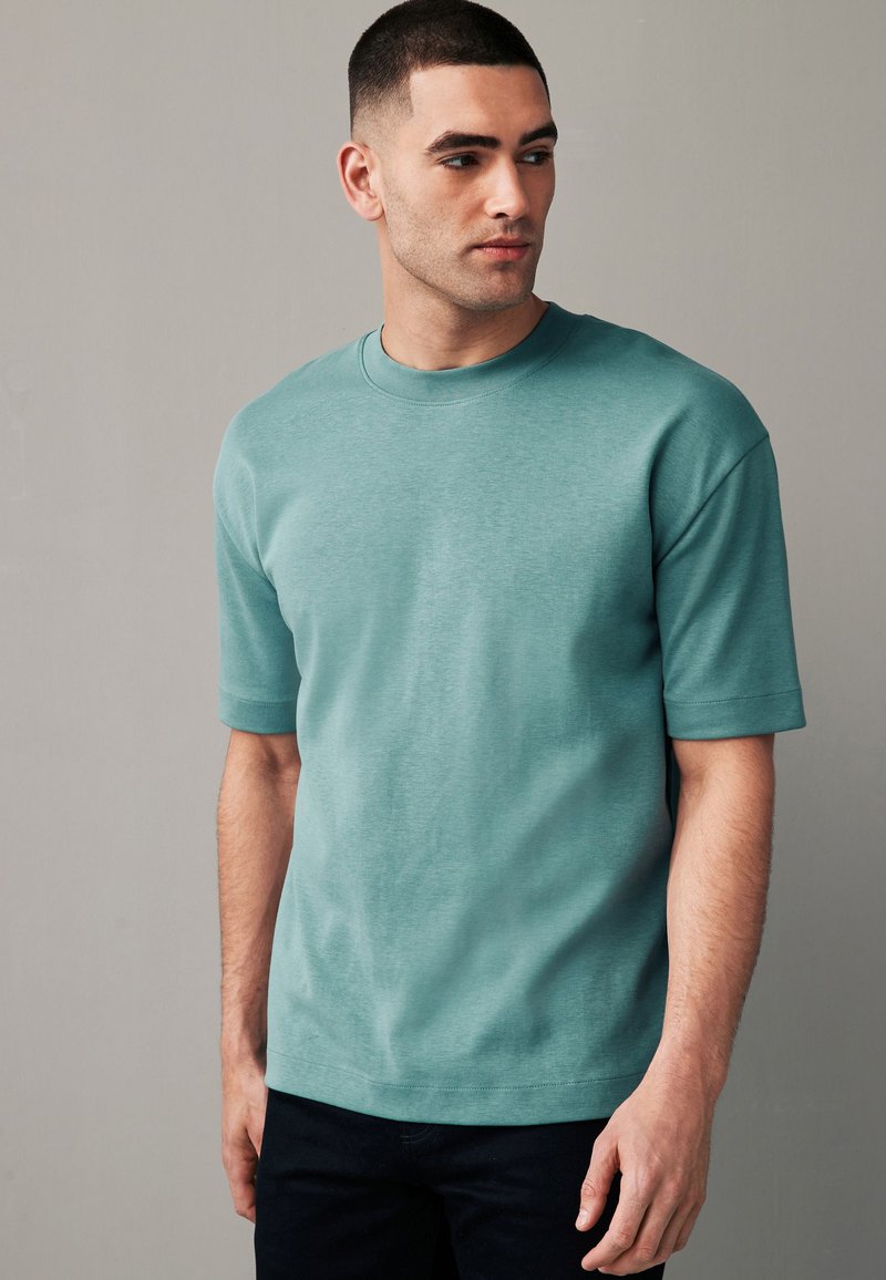 Kurzarm-T-Shirt in gedämpftem Türkis aus weichem Stoff; runder Halsausschnitt; lässiger Schnitt mit minimalen Nähten und Branding.