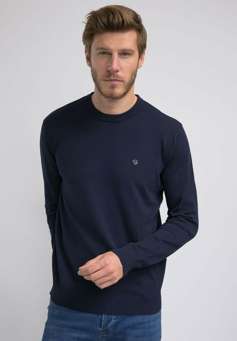 Pull à col rond bleu marine en tissu doux, doté d'un ourlet et de manches côtelés, avec un petit logo en accent sur la poitrine.