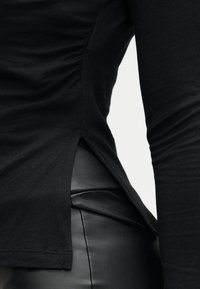 Μαύρο τοπ με μακριά μανίκια, ρελιασμένο πλαϊνό με πιέτες και πλαϊνές σχισμές, σε συνδυασμό με εφαρμοστά μαύρα παντελόνια από συνθετικό δέρμα. Υφή υφάσματος και κομψός σχεδιασμός.