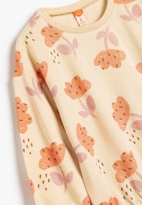 Sudadera de color beige claro con un patrón floral en durazno y lavanda, con mangas cortas y un cuello acanalado para añadir textura.
