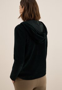 Hoodie en velours côtelé vert foncé avec une texture douce, présentant une capuche froncée et des manches longues, vu de l'arrière.