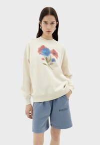 Crème sweatshirt met een bloemenprint in blauw en rood, gecombineerd met lichtblauwe shorts met een logodetail. Zachte stof, relaxte pasvorm.
