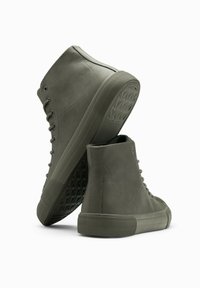 Vysoké tenisky z tmavě zelené kůže, s texturovanými gumovými podrážkami, kulatou špičkou a tkaničkami, s minimalistic designem a bez viditelných log.