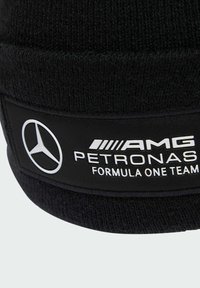 Berretto di maglia nera con una texture morbida, caratterizzato da una fascia in tessuto nera con l'iscrizione bianca "AMG PETRONAS" e logo, progettato per i fan della Formula Uno.