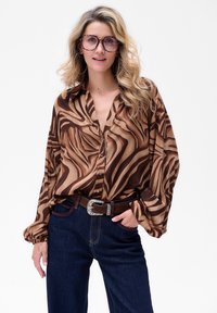 Bruine en beige gebloemde blouse met knoopsluiting aan de voorkant, ballonsleeves, gecombineerd met donkerdenim jeans en een bruin riem met zilveren accenten.