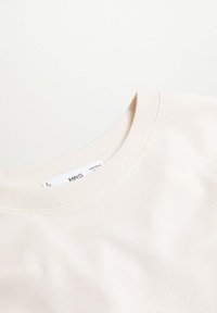 Sweat-shirt écru à col rond avec col côtelé et étiquette de marque MNG visible à l'intérieur du col.