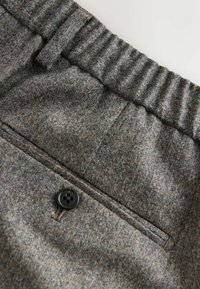 Graue Wollhose mit elastischem Bund, ausgestattet mit einem einzelnen schwarzen Knopf an der Gesäßtasche und einer glatten Textur.