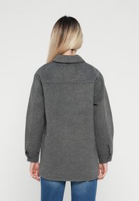Grå ullblandad jacka med krage, knappade manschetter och avslappnad passform. Har en mjuk textur och en längre bakdel.