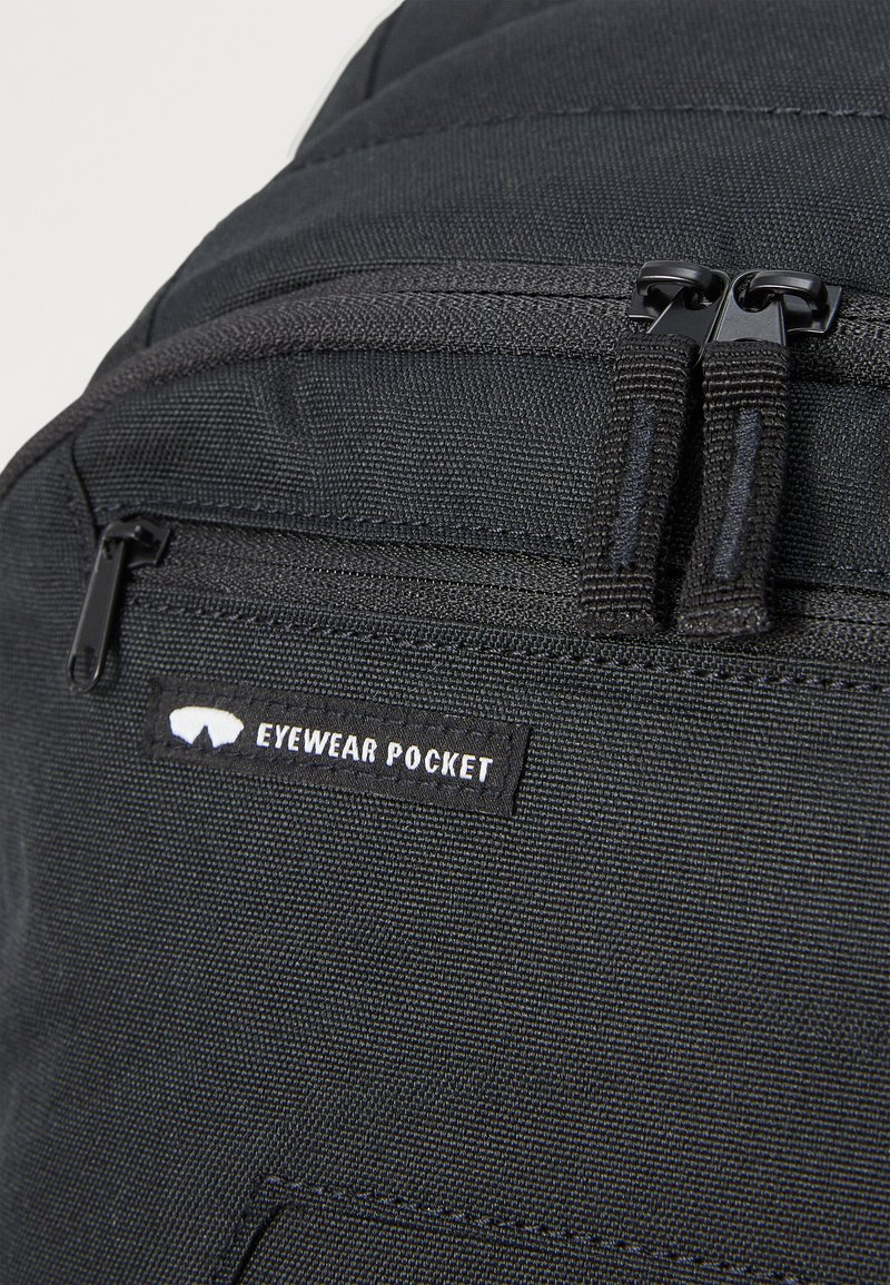 Zwarte stoffen rugzak met een ritsen brilvak. Beschikt over duurzaam materiaal, een gestructureerd oppervlak en een genaaid label met witte letters.