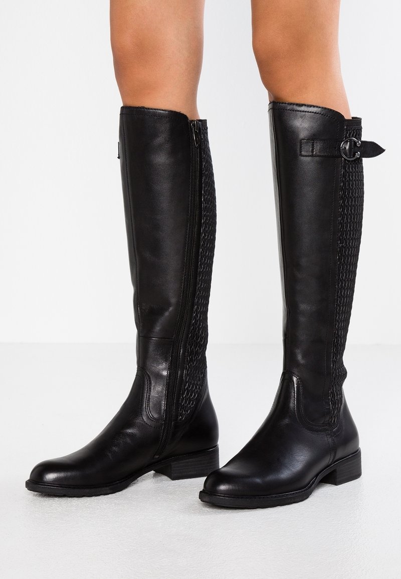 Bottes noires en cuir arrivant au genou avec une fermeture éclair sur le côté, un panneau texturé noir, un petit talon épais et un accent en sangle au niveau du mollet.