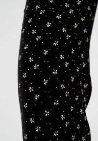 Tissu en velours noir avec un motif floral doré et des points. Gros plan montrant la texture et le détail du design du matériau.