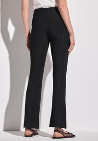 Pantaloni neri a costine svasati con un alto punto vita e due tasche posteriori. Il materiale ha una finitura testurizzata; abbinati a scarpe piatte con cinturini.