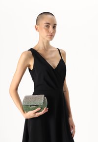 Kryštálmi zdobená kabelka v obdĺžnikovom tvare, so zeleným základom a striebornými kamienkami. Nosí sa s elegantnými čiernymi šatami.
