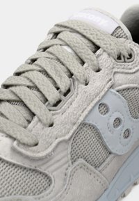 Grauer Sneaker aus Wildleder und Mesh mit drei runden Akzenten, strukturierten Schnürsenkeln und einem hellblauen Logo-Patch auf der Zunge. Design mit niedrigem Schnitt.