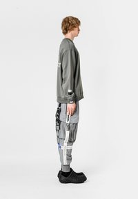 Sudadera gris de manga larga, combinada con pantalones cargo grises que presentan varias correas y etiquetas, y zuecos texturizados negros.