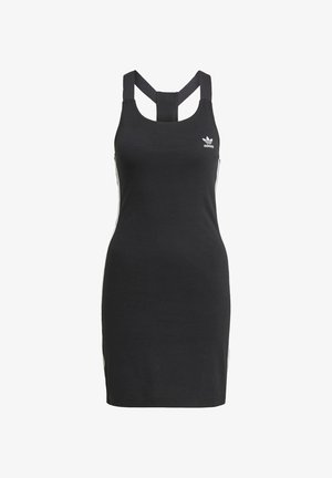 Spijkerjack, zwarte jurk met zijstrepen en witte sneakers. Het jack heeft knoopsluitingen en opgerolde mouwen. Eenvoudige, casual outfit.