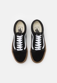 Pár černých sneakers Vans s bílými šňůrkami a bočním pruhem, gumovými podrážkami, pohled shora na bílém pozadí.