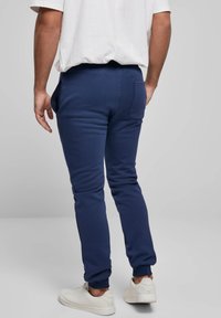 Tamsiai mėlyni treningai iš minkšto medvilnės mišinio, siaurėjantys dizainu, su šoniniais kišenėmis, raišteliais rankogaliuose ir detalė ant nugaros kišenės.